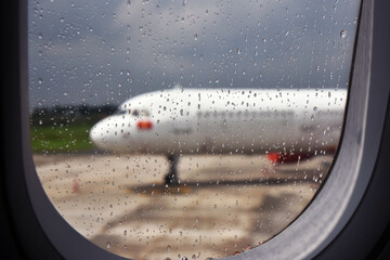 The view from the window, covered with raindrops, on the blurred silhouette of a white plane