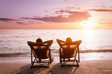 Young spouses couple sitting in deck chairs on sea beach and looking on sun. Luxury honeymoon...
