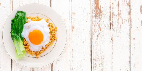 stir fried spicy instant noodles with bok choy topped with fried egg in ceramic plate on white wood texture background with copy space for text, top view, flat lay, 2 x 1 ratio