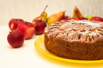 Charlotte apple pie cooked home with powdered sugar on yellow plate with apples and pears in background