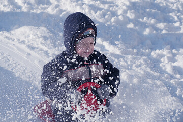 Fototapeta na wymiar Boy sledding down on snow hill in winter