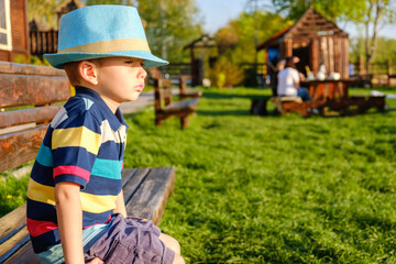 Smiling child sitting on a park bench with green meadow on background