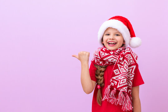 A little girl in a Christmas outfit smilingly points her fingers at an advertisement and an advertising banner.