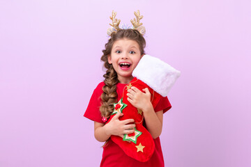 The little girl is wearing children's Christmas horns and she is holding a bag of gifts in her hands.
