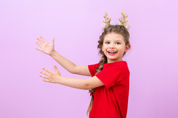 A funny little girl in a Santa Claus hat shows her hands to the side on an isolated background.
