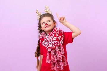 A dressed up little girl with deer ears on her head points her finger up and smiles.