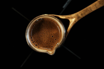 Fresh hot coffee in copper cezve on black surface of an induction slab. Top view.