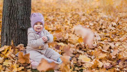 Little cheerful girl sits under a tree in autumn yellow foliage. Copy space