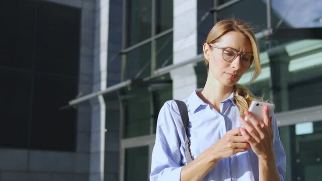 Concentrated woman in casual shirt with blond hair reading message on smartphone with serious face expression, receiving bad or important news, thinking over information, pondering about next actions