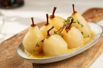 Peeled poached pears with caramel sauce on a white oval plate on a wooden board