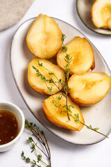 Caramelized pear halves on an oval grey plate with thyme branches and caramel on a white table surface