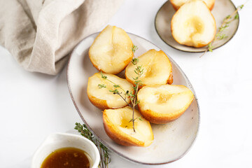 Caramelized pear halves on an oval grey plate with thyme branches and caramel on a white table...