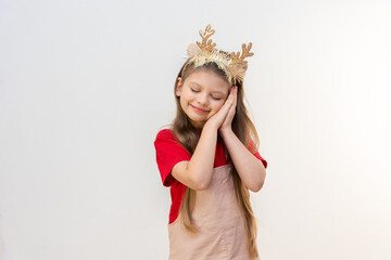 A little girl with Christmas horns has her hands under her cheek and is sleeping.
