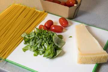 Spaghetti, tomatoes, parmesan and basil on a board