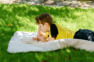 Cute blond little kid boy reading book in garden, outdoors. Excited school child reading loud....