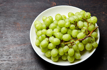 Branch of ripe green grape on plate with water drops. Juicy grapes on wooden background, closeup. Grapes on dark kitchen table with copy space