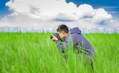 Naklejka na ściany i meble Man taking picture with camera in the field, photographer in the field taking a picture, Latino man in a green field taking a picture