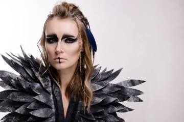 Beautiful woman in makeup and costume for halloween on a white background. Fantasy image of a harpy...