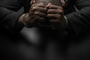 A businessman in a black suit puts handcuffs on the table and the black table. Corruption, bribery,...