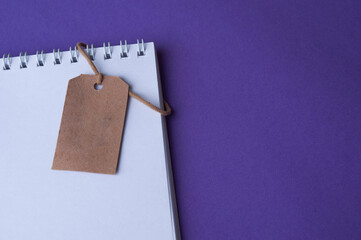 Blank notebook isolated on purple background with hanging tag. Top view. Copy space.