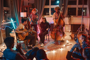 Young people playing musical instruments and singing while gathering together in music studio