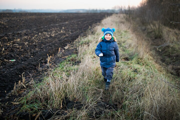 Little preschool boy running in winter clothes along the field in village