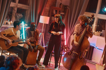 Young woman singing while her band playing musical instruments during their performance in the club