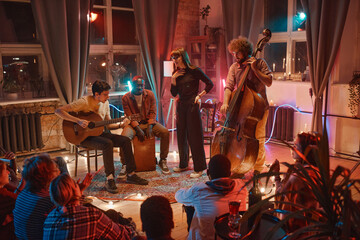 Group of young people playing musical instruments and singing during performance for people in the...