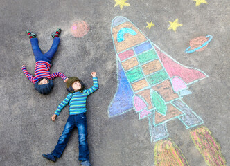 Two little kids boys having fun with drawing universe and space shuttle picture with colorful...