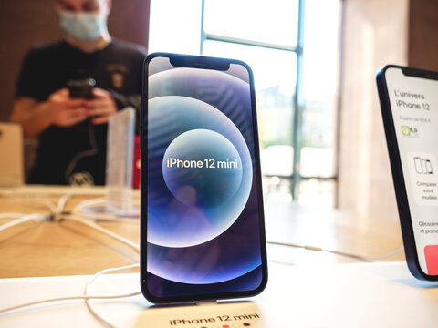 Paris, France - Sep 24, 2021: New Apple iPhone 12 mini for sale in Apple Store with customer with mask testing the telephone in background