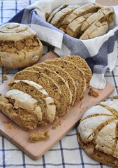 Round loaves of rustic bread on a blue and white square patterned dishcloth with two of the loaves cut into slices