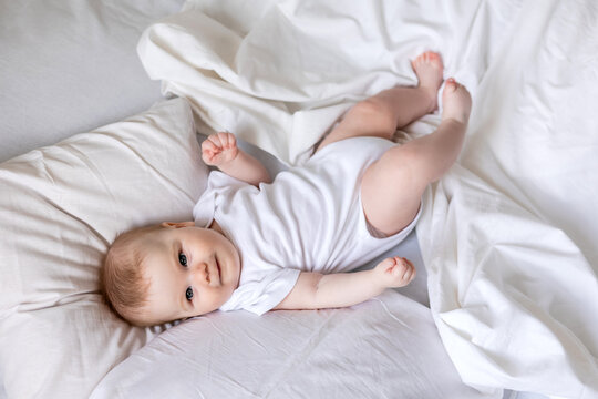 baby in a white bodysuit is lying on his back in a bed made with white bed linen. children's sleep and rest. concept of a happy childhood and motherhood. lifestyle, space for text. High quality photo
