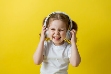 portrait of a cute cheerful little girl listening to music with white headphones. audiobooks, audio lessons. concept of education. photo studio, yellow background, text space. High quality photo