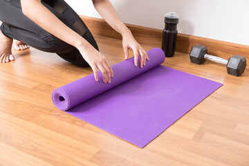 Fototapeta na wymiar Close-up of woman hands rolling purple yoga mat for playing yoga at home from Covid-19, New normal lifestyle concept.