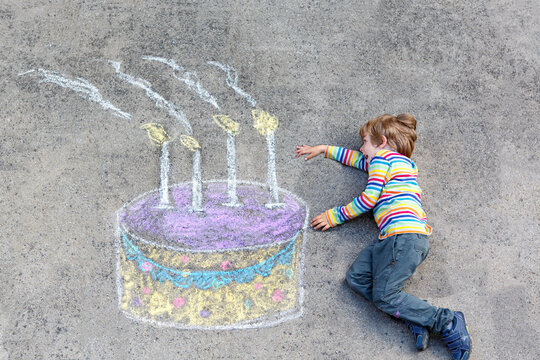 Happy little kid boy having fun with big birthday cake picture drawing with colorful chalks. Creative leisure activity for children outdoors in summer. Child celebrating birthday and drawing on ground
