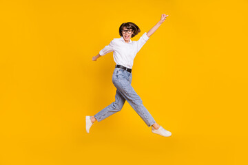 Fototapeta na wymiar Photo of cheerful hero lady jump raise fist wear specs white shirt jeans sneakers isolated yellow color background