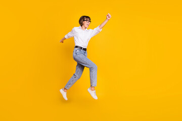 Fototapeta na wymiar Profile photo of savior lady jump run raise fist wear eyewear white shirt jeans footwear isolated yellow color background