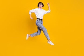Fototapeta na wymiar Photo of positive lucky funny lady jump run wear spectacles white shirt jeans shoes isolated yellow color background