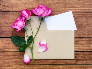 Bouquet of pink roses in an envelope on a wooden background. Postcard with place for design.