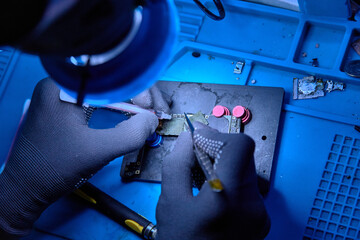 Hands in gloves of professional technician repairman work on chipset pins of removed microprocessor from smartphone motherboard. Close-up macro photo, Selective focus