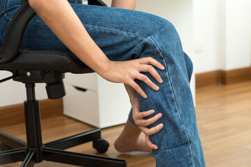 Young woman sits in an office chair massages her tired leg, leg pain.