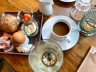 Table laid for breakfast outside in summer with various jams, bread, coffee, croissants, eggs, bacon muesli and orange juice
