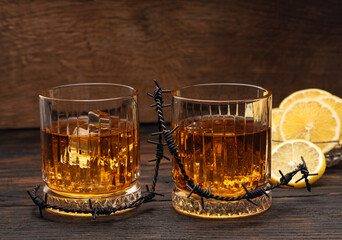 Whiskey or cognac or bourbon with ice on a wood background with lemon wedges