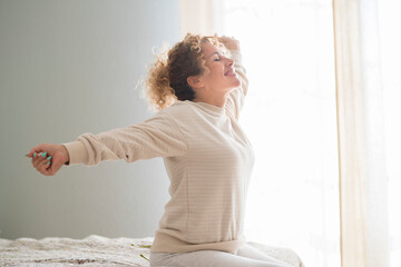 Beautiful caucasian young woman with curly hair enjoying sunny morning on bed. Smiling young woman...