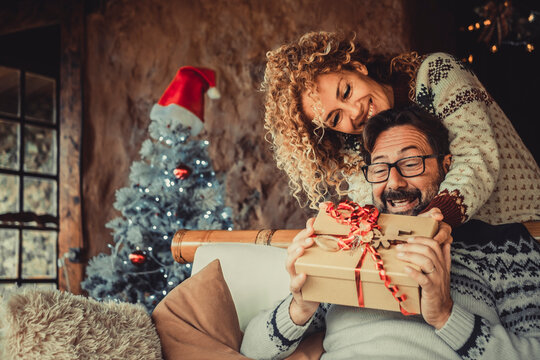 Overjoyed Man Receive Christmas Gift From His Wife. Happy People Enjoy And Celebrate Christmas Eve At Home. Xmas Tree In Background. Winter Leisure Couple Lifestyle Indoor