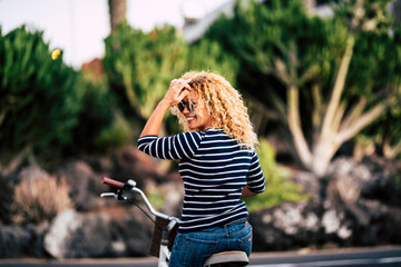 Hipster woman with curly hair and sunglasses sitting on bicycle looking over shoulder and admiring...