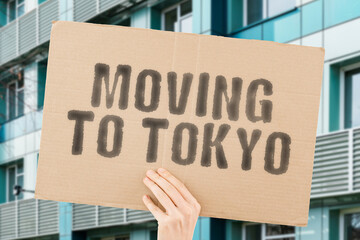 The phrase " Moving to Tokyo " drawn on a carton banner in men's hand. Human holds a cardboard with an inscription. Big city. Urban. Opportunity. Immigration
