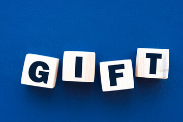 The hand puts a wooden cube with the letter T from the word Gift. The word is written on wooden cubes standing on the white surface of the table. Communication and business concepts