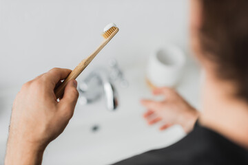 Blurred man holding toothbrush and toothpaste in bathroom