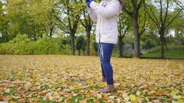 Asian woman taking a photo of view at park. Walking around with Autumn outfits, Good weather, yellow leaves falling on the grass. A lot of tree background, Stockholm, Sweden in Autumn concept
